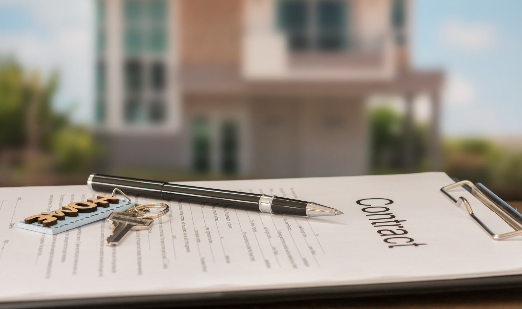 closeup pen on contract document with house key in house background.